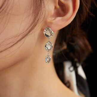 Close-up view of a woman's ear adorned with a long, gold earring with three interlocking rings against a dark background. Elegant pearl jewelry