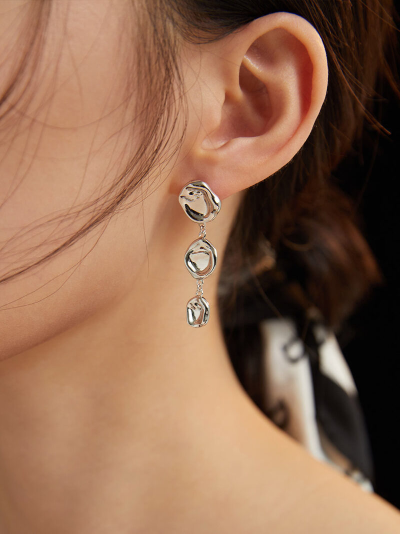 Close-up view of a woman's ear adorned with a long, gold earring with three interlocking rings against a dark background. Elegant pearl jewelry