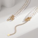 Two strands of pearls with golden clasps lie on a white surface, casting soft shadows in the sunlight, adjacent to a delicate gold chain with a small pendant. Elegant pearl jewelry