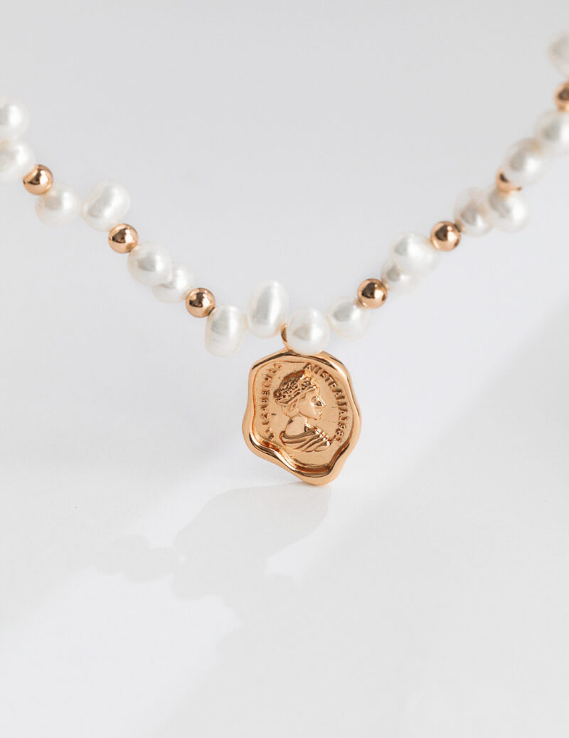 Elegant necklace featuring a string of pearls and rose gold beads, with a central rose gold pendant engraved with a detailed classical profile. Elegant pearl jewelry