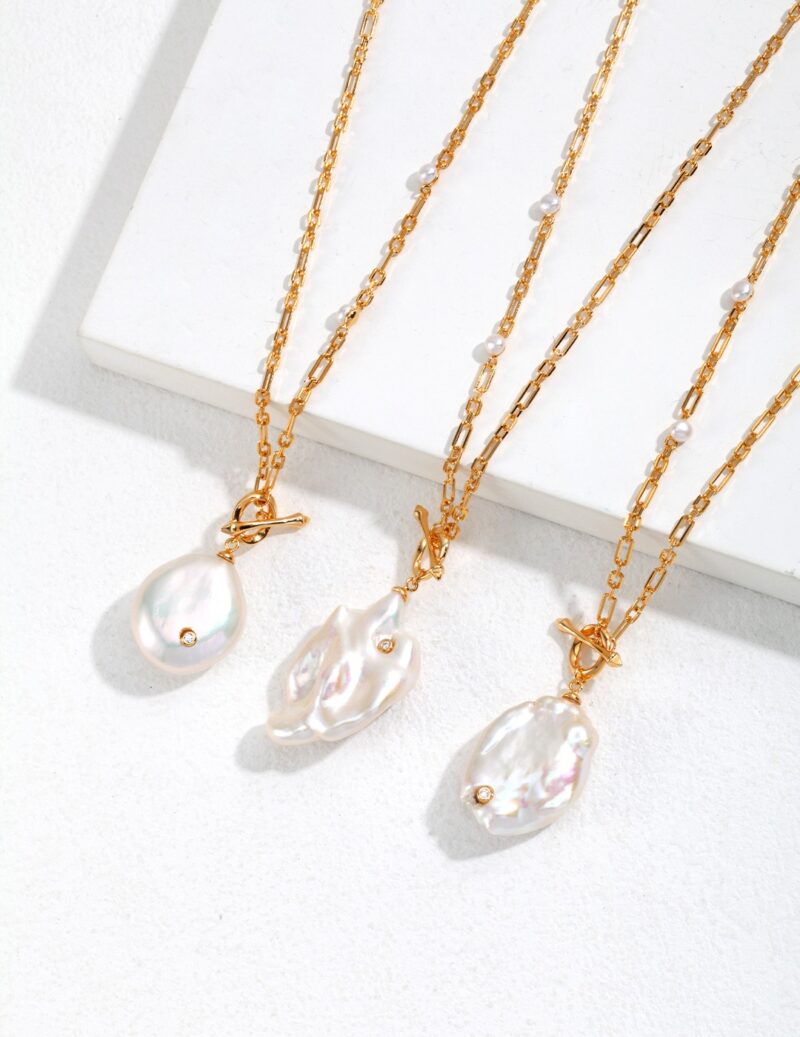 Three elegant necklaces with freshwater pearl accents hanging over the edge of a white display, each featuring a unique baroque pearl pendant, highlighted by soft, natural light. Elegant pearl jewelry