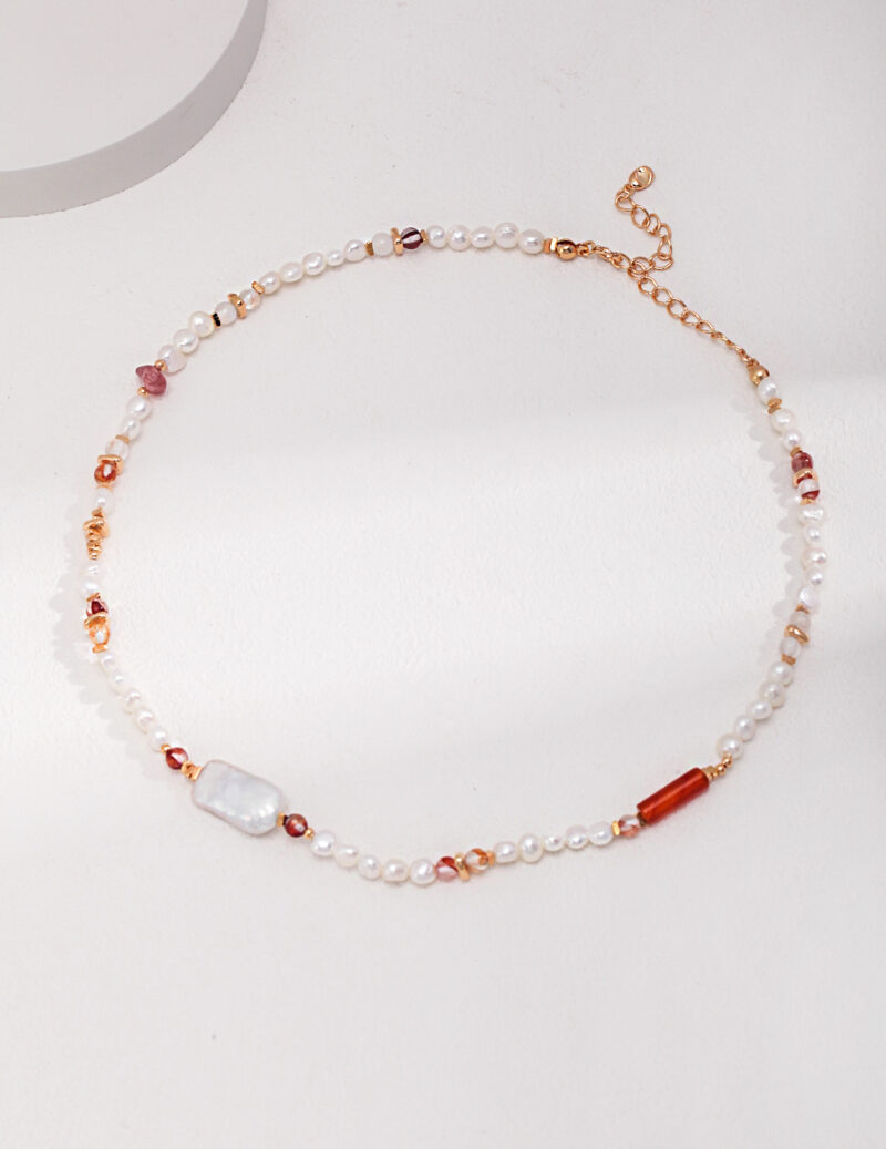 An elegant necklace featuring pearls and a mix of translucent and amber-toned gemstones, highlighted by rose gold accents, laid upon a white surface.