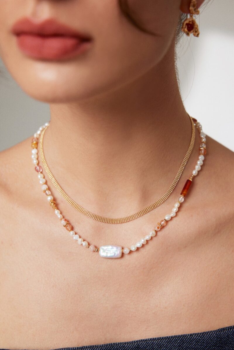 Close-up of a woman wearing an elegant necklace with a large rectangular freshwater pearl centerpiece, complemented by subtle makeup and a stylish earring. Elegant pearl jewelry