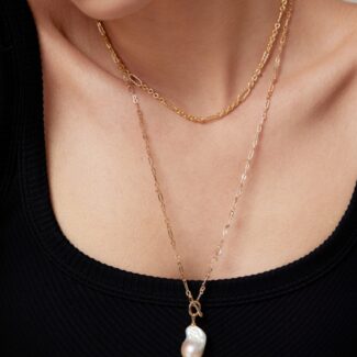 Close-up of a woman wearing a black top and two necklaces, one with a pendant featuring a large freshwater pearl, set against a neutral background. Elegant pearl jewelry