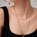 Close-up of a woman wearing a black top accessorized with layered gold necklaces and earrings, focusing on her elegant jewelry. Elegant pearl jewelry