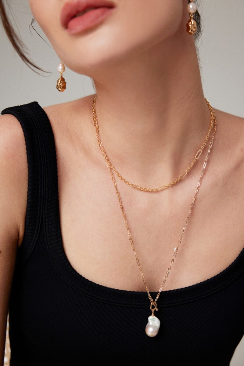 Close-up of a woman wearing a black top accessorized with layered gold necklaces and earrings, focusing on her elegant jewelry. Elegant pearl jewelry