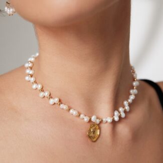 Close-up of a woman wearing necklace with a golden pendant, focusing on the necklace. Part of her lips are visible against a soft-focus background. Elegant pearl jewelry