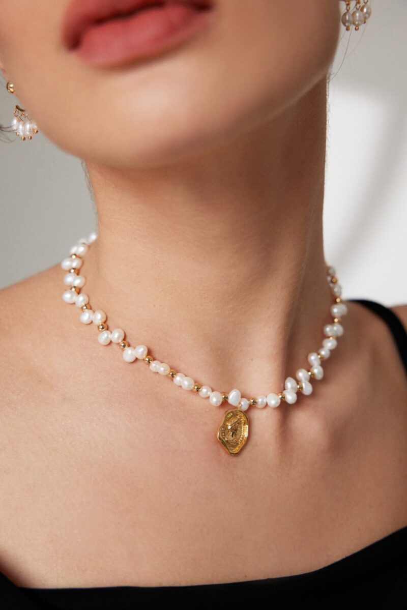 Close-up of a woman wearing necklace with a golden pendant, focusing on the necklace. Part of her lips are visible against a soft-focus background. Elegant pearl jewelry