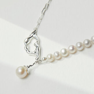 A delicate necklace with a twisted pendant and a string of freshwater pearls ending in a larger dangling natural pearl, laid out on a bright, textured surface. Elegant pearl jewelry