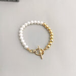 A bracelet made of alternating white pearls and gold beads, featuring a gold toggle clasp, displayed on a light gray surface with gold pearl jewelry. Elegant pearl jewelry