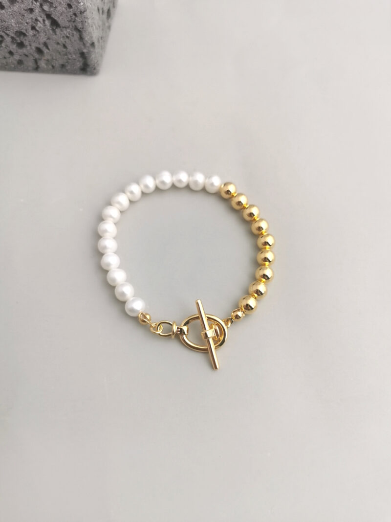 A bracelet made of alternating white pearls and gold beads, featuring a gold toggle clasp, displayed on a light gray surface with gold pearl jewelry. Elegant pearl jewelry