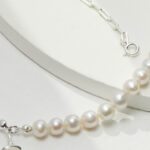 A close-up image of jewelry with a silver chain on a white display background, highlighting the lustrous pearls and the shiny metal clasp. Elegant pearl jewelry