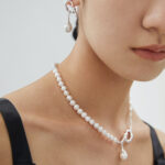 Close-up of a person wearing a necklace and matching earrings, showcasing elegant jewelry against a neutral background. Focus on the smooth natural pearls and shiny silver clasp. Elegant pearl jewelry