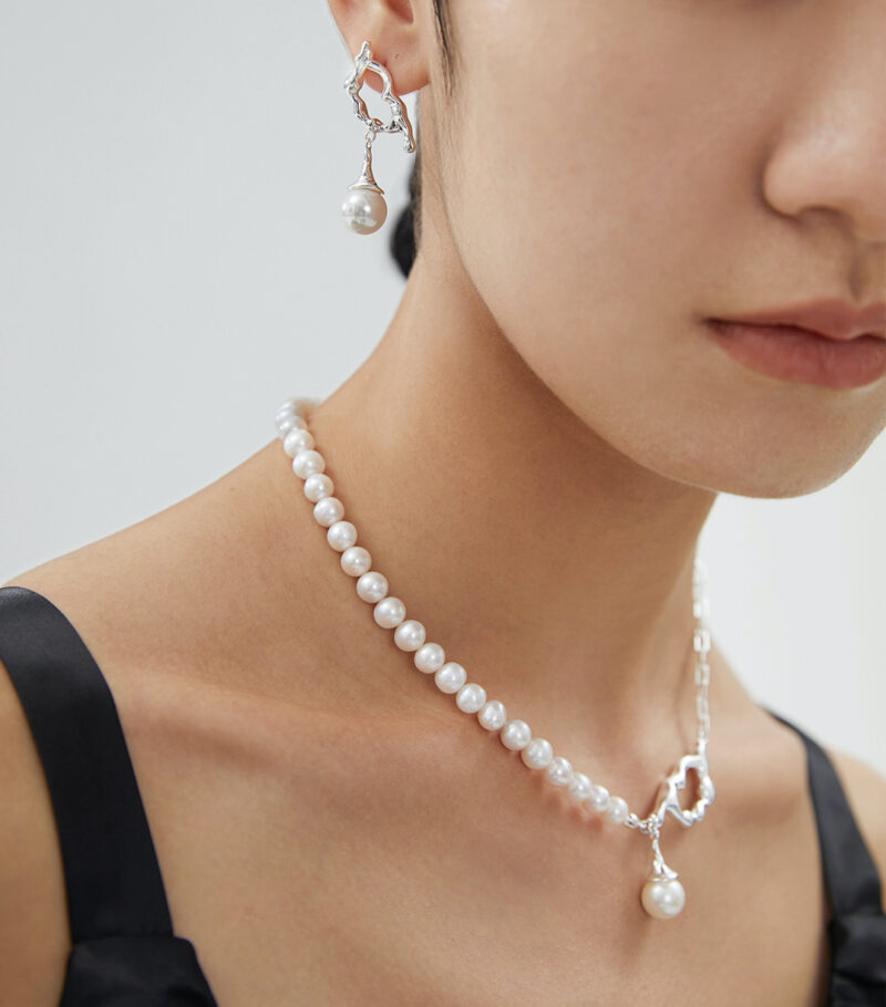 Close-up of a person wearing a necklace and matching earrings, showcasing elegant jewelry against a neutral background. Focus on the smooth natural pearls and shiny silver clasp. Elegant pearl jewelry