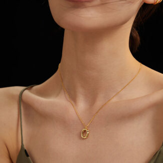 Close-up of a woman's neck wearing a delicate necklace with an oval pendant, adorned with natural pearl, against a dark background. Her dress has thin straps and her hair is windswe Elegant pearl jewelry