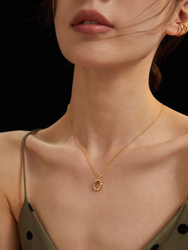 Close-up of a woman's neck wearing a delicate necklace with an oval pendant, adorned with natural pearl, against a dark background. Her dress has thin straps and her hair is windswe Elegant pearl jewelry