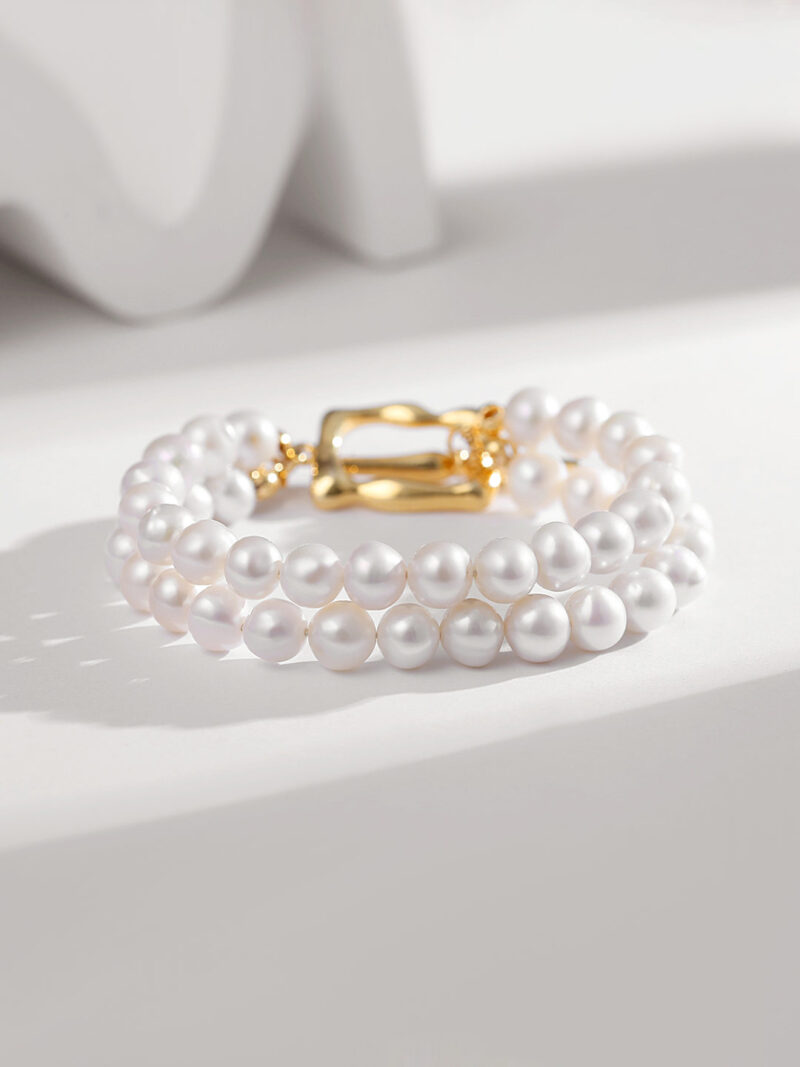 Elegant featuring multiple strands of pearls with a gold clasp, highlighted by a soft, shadowed white background. Elegant pearl jewelry