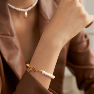 A close-up photo of a woman wearing a brown leather jacket, featuring pearl jewelry including a bracelet on her wrist and a necklace around her neck. Elegant pearl jewelry