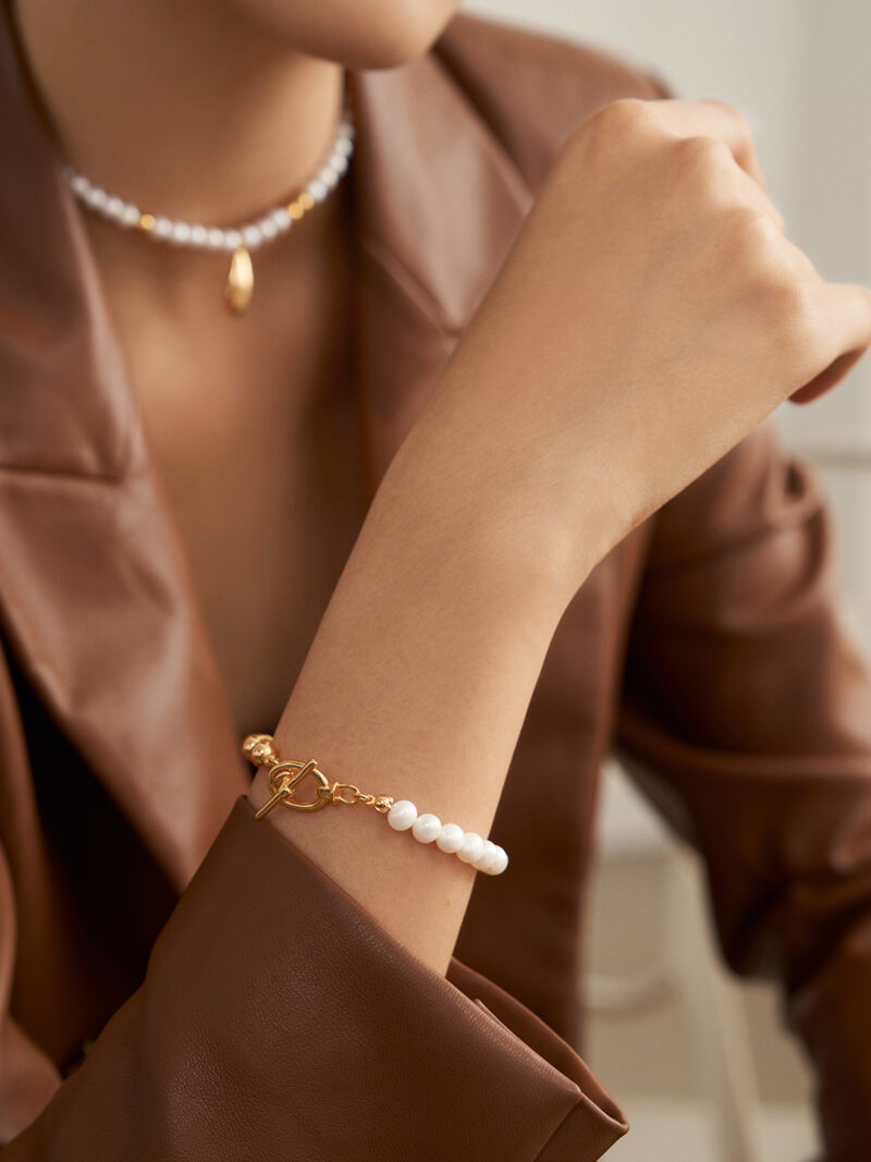 A close-up photo of a woman wearing a brown leather jacket, featuring pearl jewelry including a bracelet on her wrist and a necklace around her neck. Elegant pearl jewelry