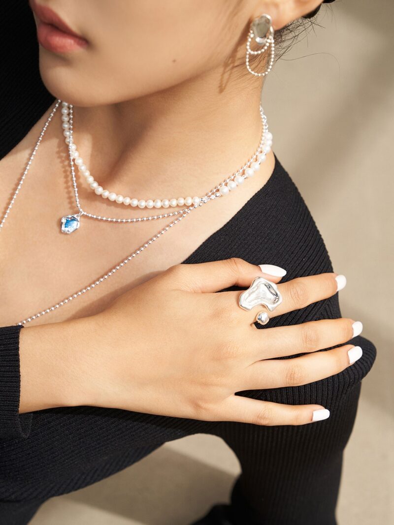 Sentence with product name: Close-up of a woman adorned with elegant gold pearl jewelry, featuring natural pearl necklaces, dangling earrings, and a prominent ring