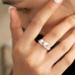 Close-up of a woman’s hand touching her face, showcasing a ring. She has manicured nails with white polish. Elegant pearl jewelry