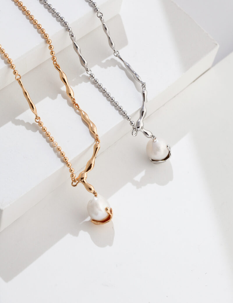 Two elegant necklaces, one  pearl jewelry and one gold pearl jewelry, draped over a white platform in bright sunlight, creating sharp shadows. Elegant pearl jewelry