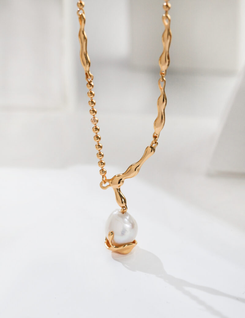 A chain necklace with an irregular link design and a single large natural pearl pendant, displayed against a softly lit white background. Elegant pearl jewelry