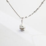 A necklace with a delicate twisted chain and a natural pearl pendant, displayed on a plain white background. Elegant pearl jewelry