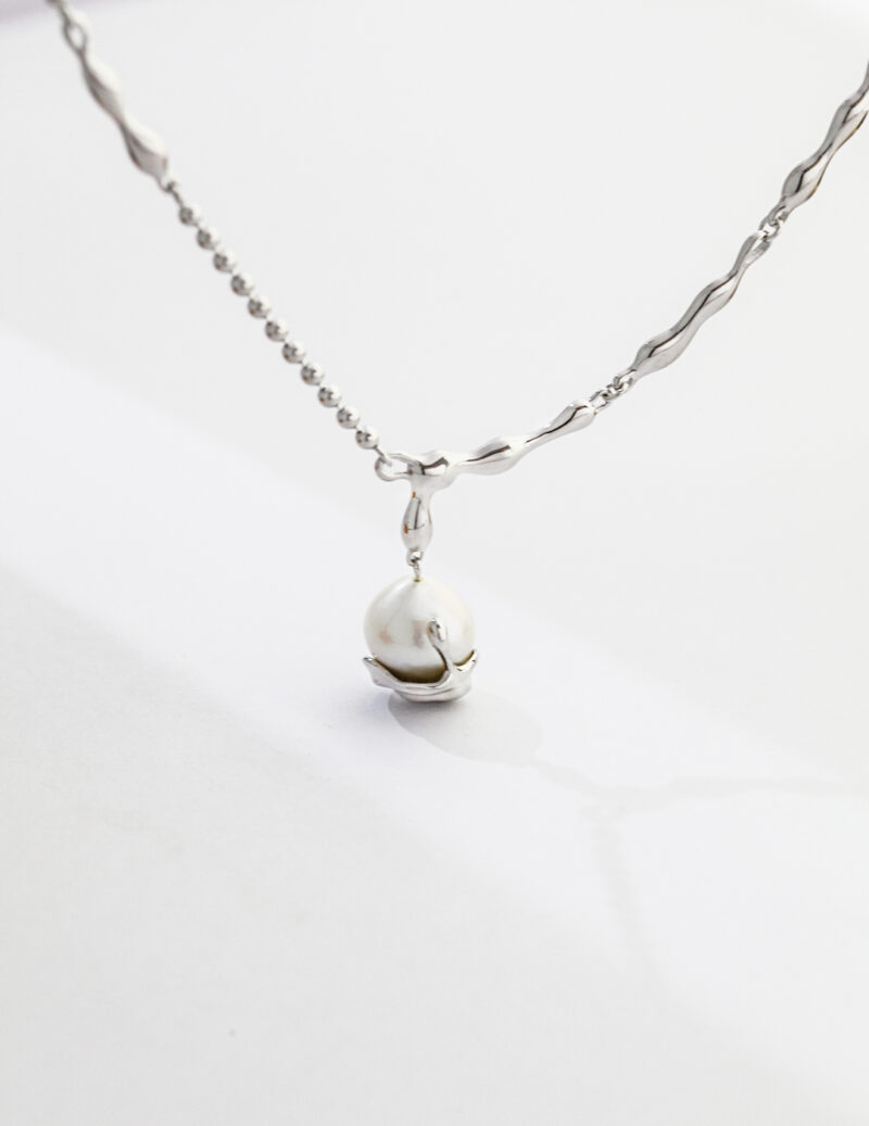 A necklace with a delicate twisted chain and a natural pearl pendant, displayed on a plain white background. Elegant pearl jewelry