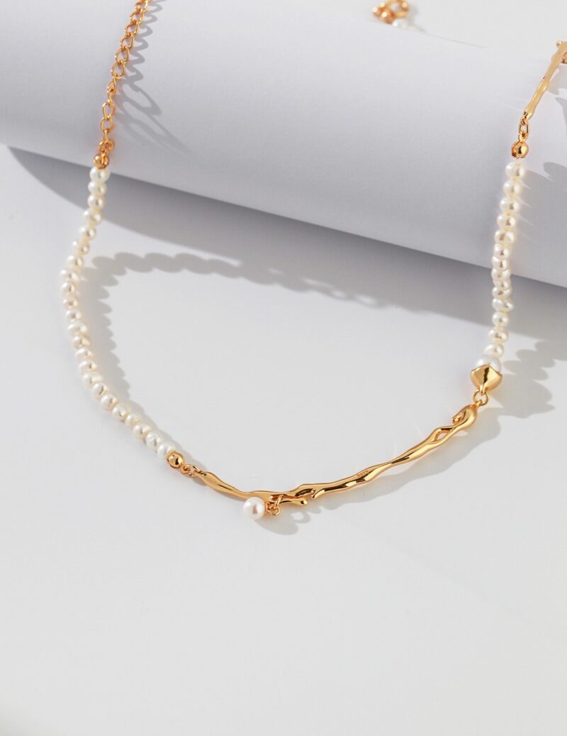 An elegant necklace with a gold chain detail, displayed on a white surface with soft shadows. Elegant pearl jewelry