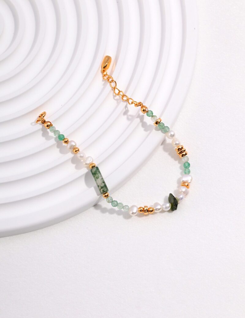 A delicate bracelet with a clasp, adorned with alternating sections of green gemstones, natural pearls, and gold accents, displayed against a white, spiraled background. Elegant pearl jewelry