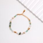 A delicate bracelet crafted with freshwater pearls, green beads, and golden clasps, displayed on a light gray surface beside a white ridged object. Elegant pearl jewelry