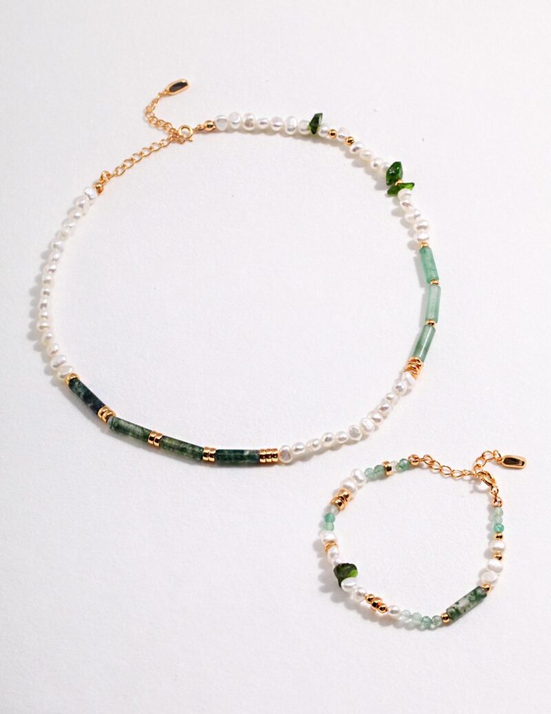 A photo of a jewelry set featuring natural pearls, green gemstones, and gold accents laid out on a white background. Elegant pearl jewelry