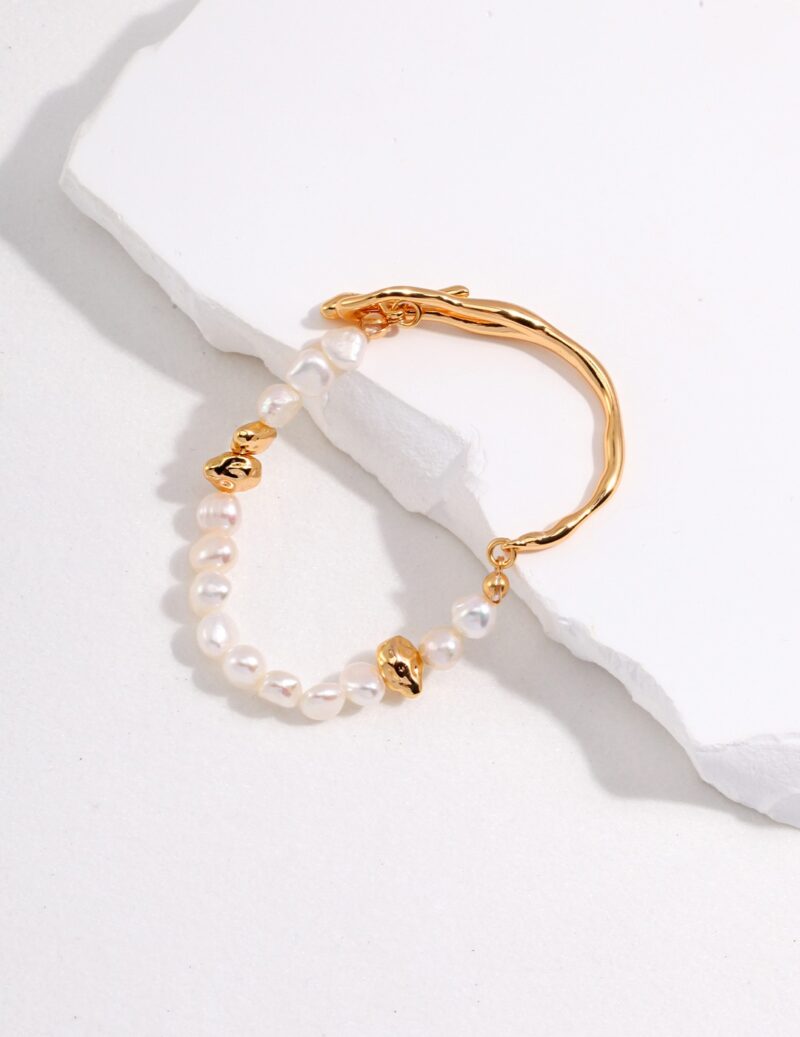 A gold hoop earring adorned with and tiny gold charms, elegantly placed on a white textured surface. Elegant pearl jewelry