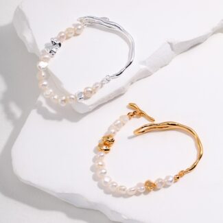 Sentence with Product Name: Two bracelets displayed on a jagged white rock surface. The top bracelet has silver accents, while the lower one features gold pearl jewelry. Elegant pearl jewelry