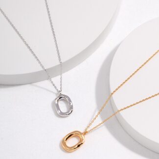 Silver and gold necklaces with abstract oval pendants featuring freshwater pearls, displayed on white, circular stands with a minimalist, shadowed background. Elegant pearl jewelry