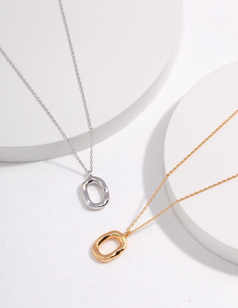 Silver and gold necklaces with abstract oval pendants featuring freshwater pearls, displayed on white, circular stands with a minimalist, shadowed background. Elegant pearl jewelry