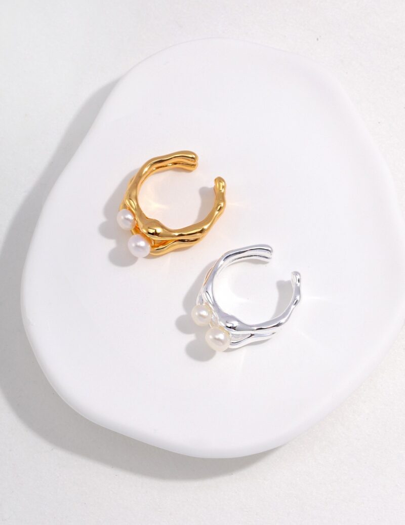 Two  rings, one gold and one silver, displayed on a white, oval-shaped surface. Elegant pearl jewelry