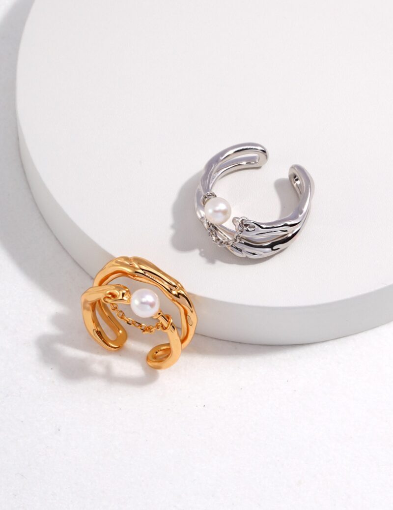 Sentence with product name: Two elegant, one gold and the other silver, each adorned with natural pearls, displayed on a circular white surface with a subtle shadow. Elegant pearl jewelry