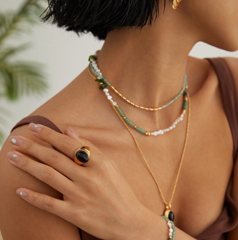 Close-up of a woman’s neck adorned with layered necklace featuring natural pearl and gold details, against a neutral background. Elegant pearl jewelry