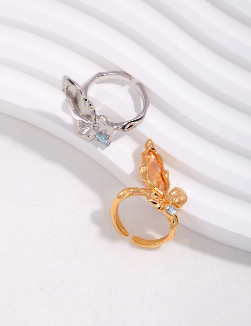 Two rings displayed on a white sculptural background. One ring is silver with a freshwater pearl in a butterfly motif, and the other is gold with a larger butterfly design featuring a natural pearl. Elegant pearl jewelry