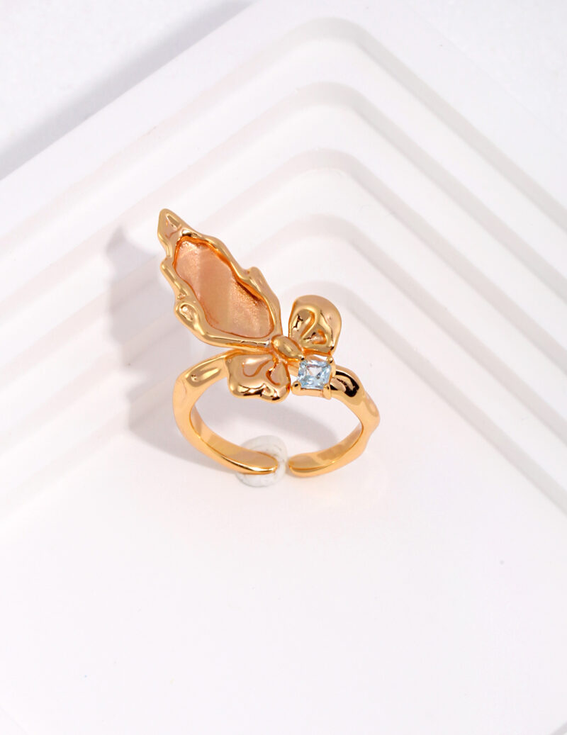 Product Name: Gold butterfly ring with a natural pearl and translucent wing detail, displayed on a white geometric surface. Elegant pearl jewelry