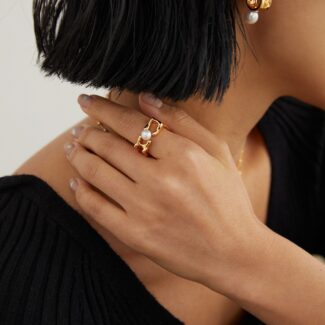 Close-up of a woman's profile from the nose down, showcasing a stylish gold pearl earring and a bold ring. She is touching her neck, set against a simple backdrop with an emphasis on o_1gg3v535ei5q1hdquai2c41aaq14r.jpg Elegant pearl jewelry