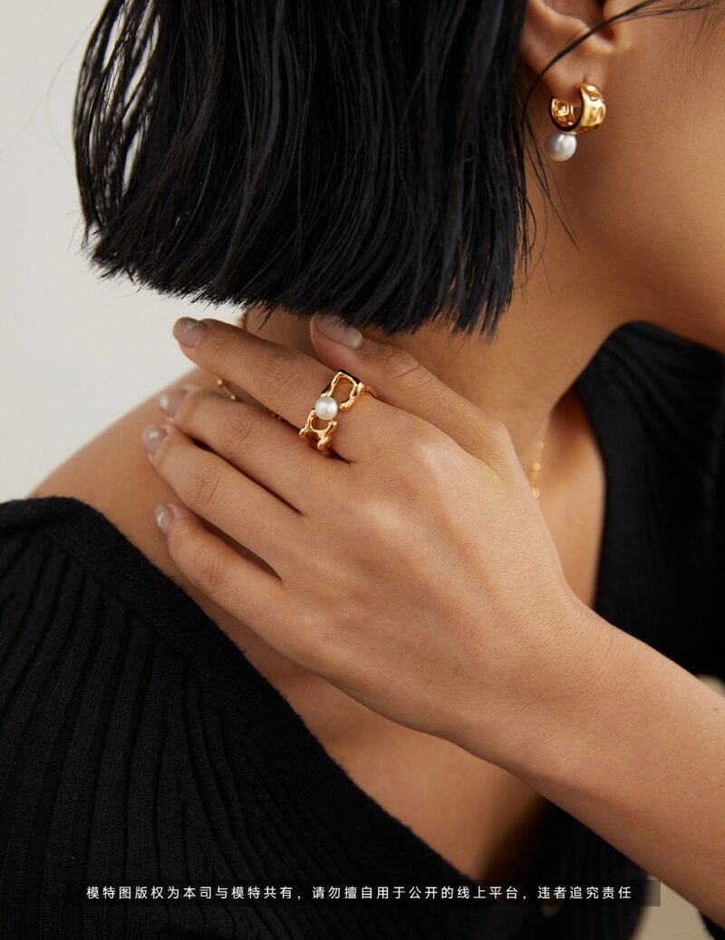 Close-up of a woman's profile from the nose down, showcasing a stylish gold pearl earring and a bold ring. She is touching her neck, set against a simple backdrop with an emphasis on o_1gg3v535ei5q1hdquai2c41aaq14r.jpg Elegant pearl jewelry