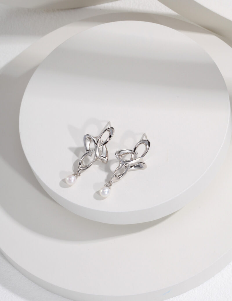 Sterling  bow-shaped earrings with freshwater pearl accents displayed on a white circular platform with a soft shadow, emphasizing the elegance and intricate design. Elegant pearl jewelry