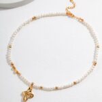 A necklace with gold accents and a treble clef charm, displayed on a white textured surface with a shadow cast by soft lighting. Elegant pearl jewelry