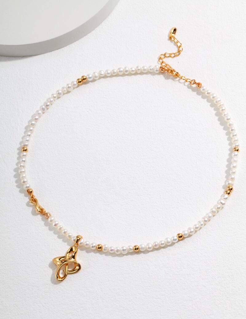 A necklace with gold accents and a treble clef charm, displayed on a white textured surface with a shadow cast by soft lighting. Elegant pearl jewelry