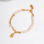 A  bracelet with a gold clasp and an ornamental charm on a white, textured surface, partially illuminated by sunlight. Elegant pearl jewelry