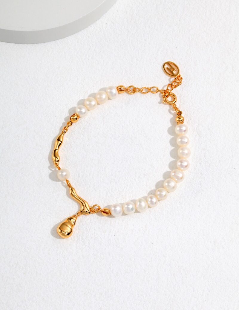 A  bracelet with a gold clasp and an ornamental charm on a white, textured surface, partially illuminated by sunlight. Elegant pearl jewelry