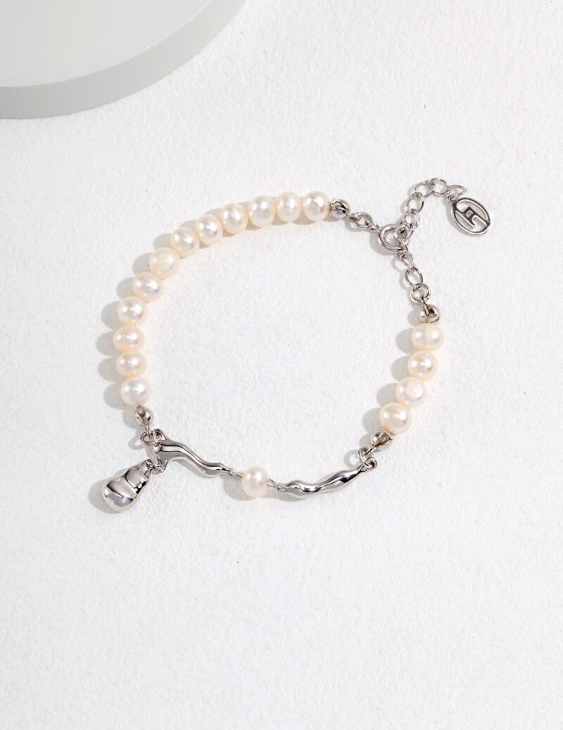 A bracelet with alternating segments of smooth natural pearls and a sterling silver chain, featuring a silver charm and clasp, displayed on a white textured surface. Elegant pearl jewelry